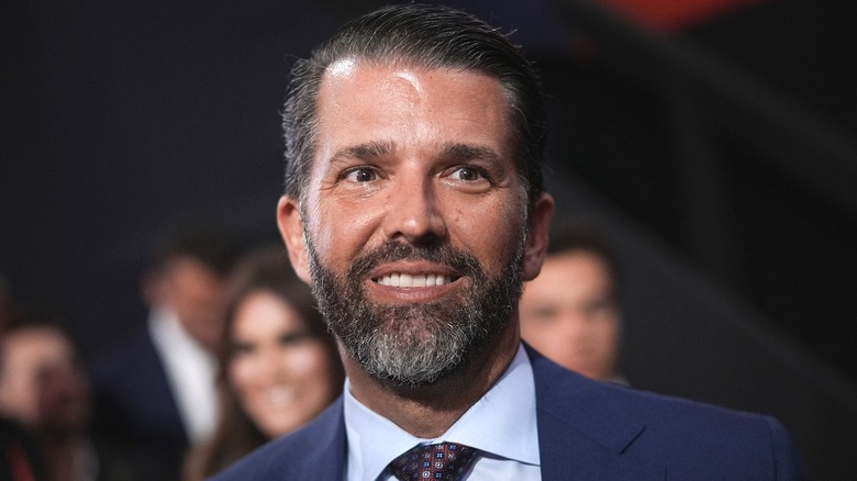 Donald Trump Jr. smiling in a navy suit