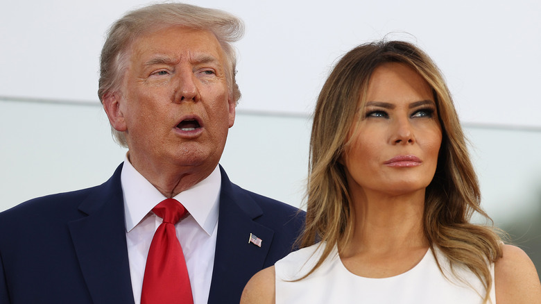 Donald Trump speaking behind Melania Trump, looking off to side