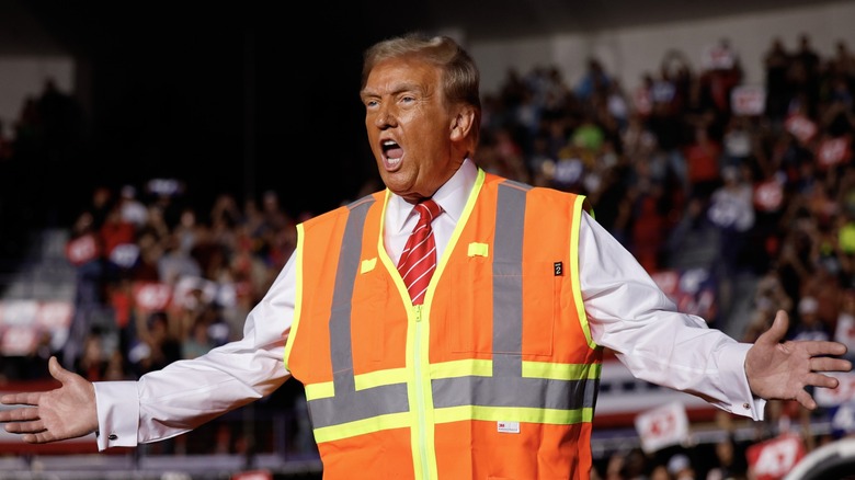 Donald Trump wearing neon orange vest, with his mouth open and arms out