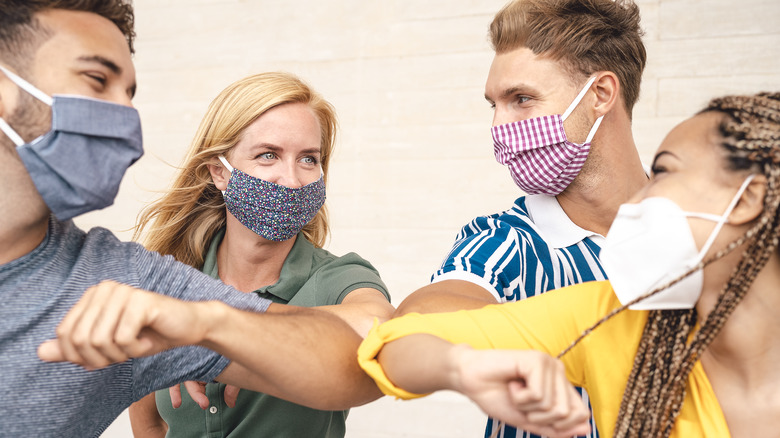 People wearing face masks elbow bump