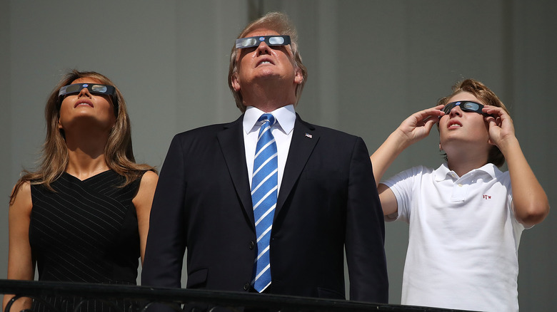 Melania Trump, Donald Trump, and Barron Trump wearing eclipse glasses on a White House balcony