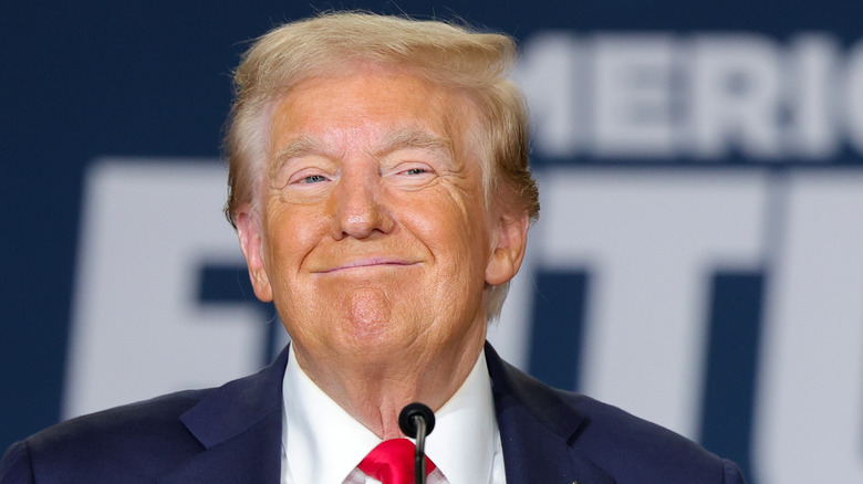 Donald Trump smiles cutely with his lips pressed together and an unnatural orange tan