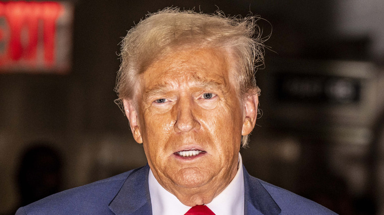 Donald Trump with an orange glow and parted lips as he speaks, his teeth are visible