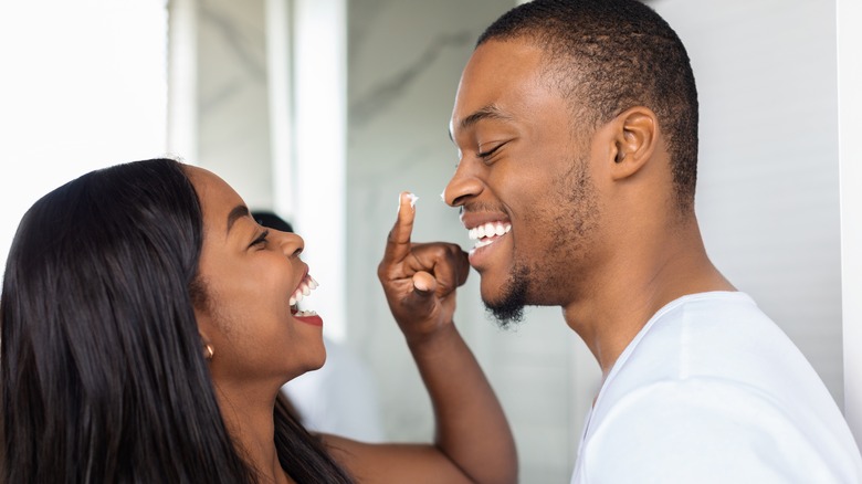 Woman playfully applying face cream on man 