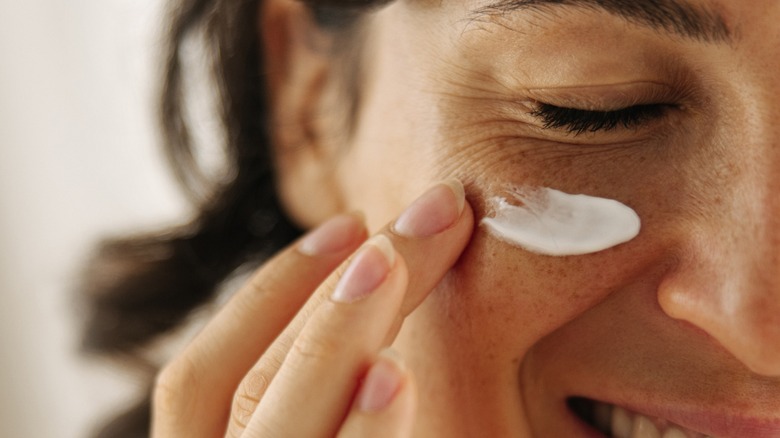 Smiling woman applying eye cream