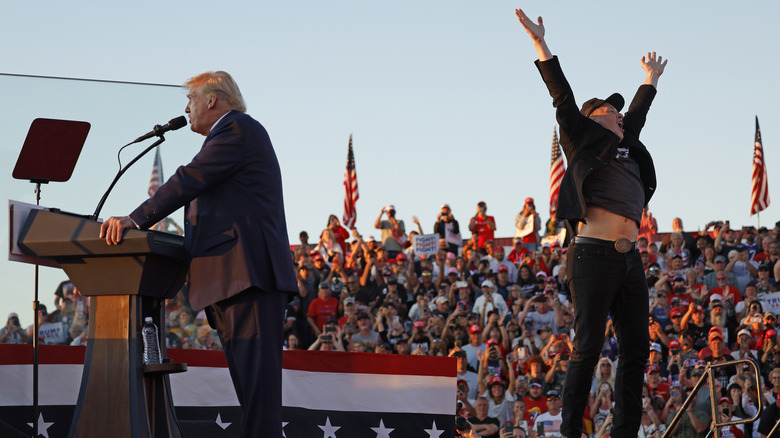 Elon Musk jumping on stage behind Donald Trump