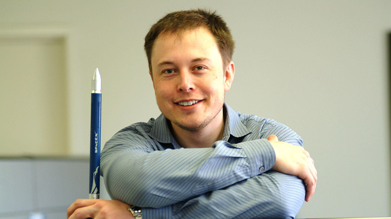 Elon Musk smiling and holding a model SpaceX rocket