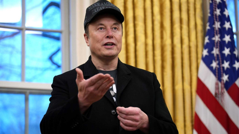 Elon Musk with MAGA hat in Oval Office gesturing