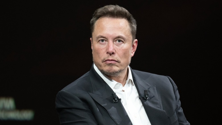 Elon Musk looking stern in a dark suit