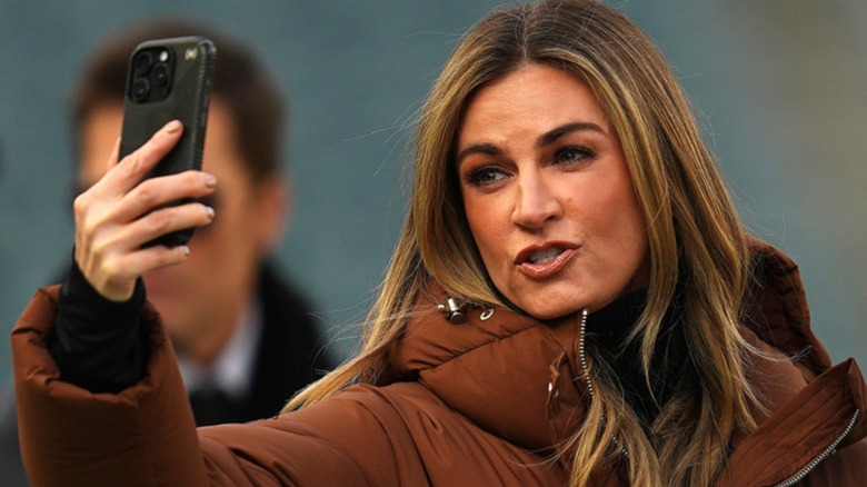 Erin Andrews wearing brown jumpsuit and filming with her phone