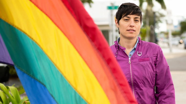 Person wearing purple jacket next to pride flag