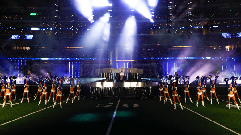 Dolly Parton onstage and Dallas Cowboys cheerleaders on field in front of her