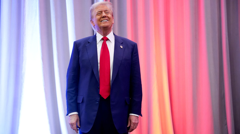 Donald Trump smiling on stage in blue suit with red tie