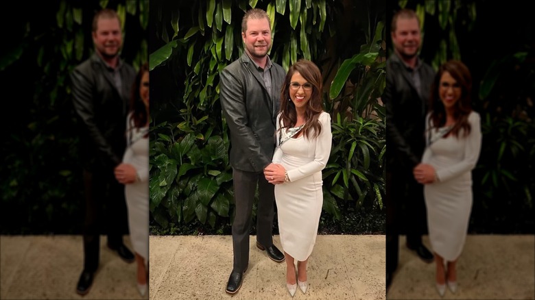 Lauren and Jayson Boebert posing together and smiling in front of greenery, hands clasped together