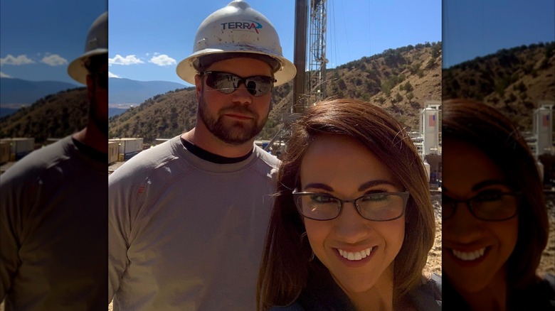 Lauren Boebert smiling while standing outside and in front of Jayson Boebert, who is wearing a hard hat and not smiling