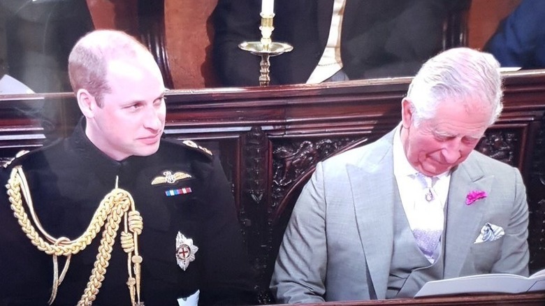 King Charles III sitting with his head bowed next to Prince William