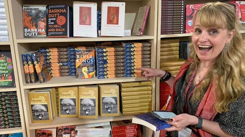 Cat Jarman standing in front of a bookshelf, pointing to her book, with a huge smile on her face.