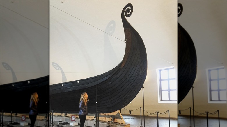 Cat Jarman in a museum, standing in front of a huge Viking ship that is taller than she is.