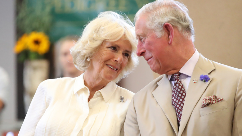 Queen Camilla leaning into King Charles talking 