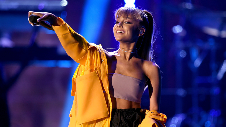 Ariana Grande on stage smiling and holding a microphone to the crowd