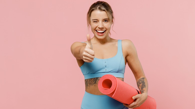 Woman holding a yoga mat showing a thumbs up