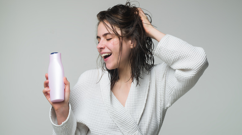 woman with damp hair holding a bottle of conditioner