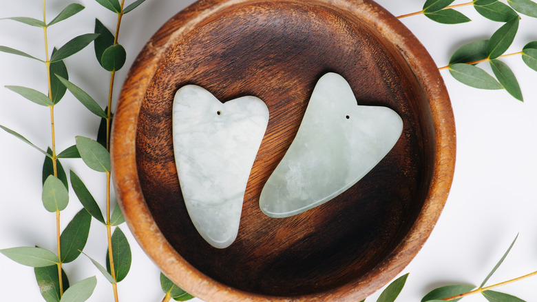 Two jade gua sha stones in a wooden bowl