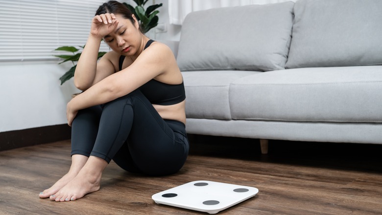 Woman upset, sitting on the floor next to a scale