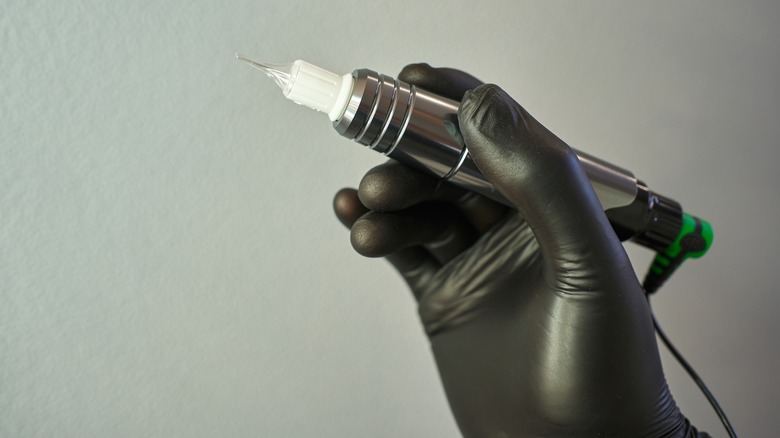 Tattoo artist in black gloves holds tattoo gun 