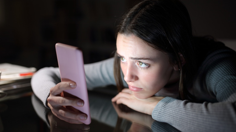 worried woman looking at her phone in the dark