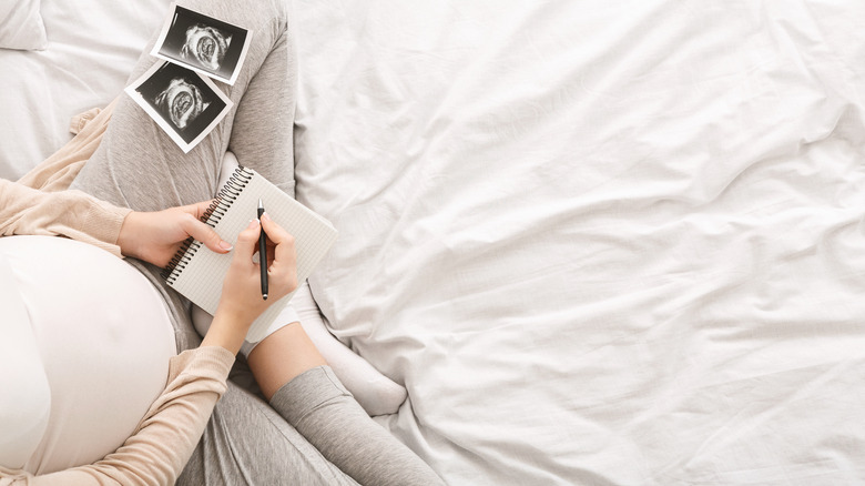 pregnant person holding notebook and sonogram photos