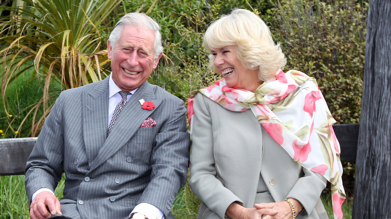 King Charles and Queen Camilla sitting laughing 