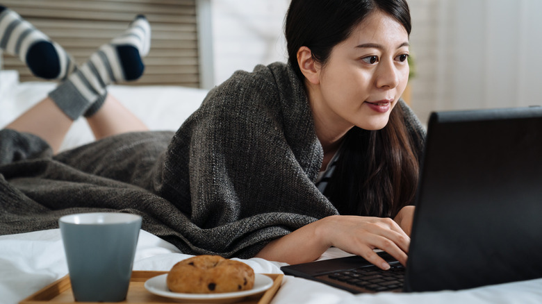 woman eating in bed on computer