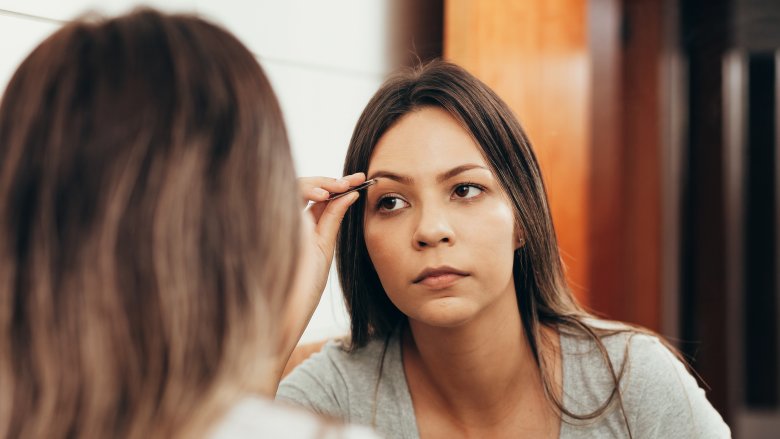 woman tweezing eyebrows in mirror