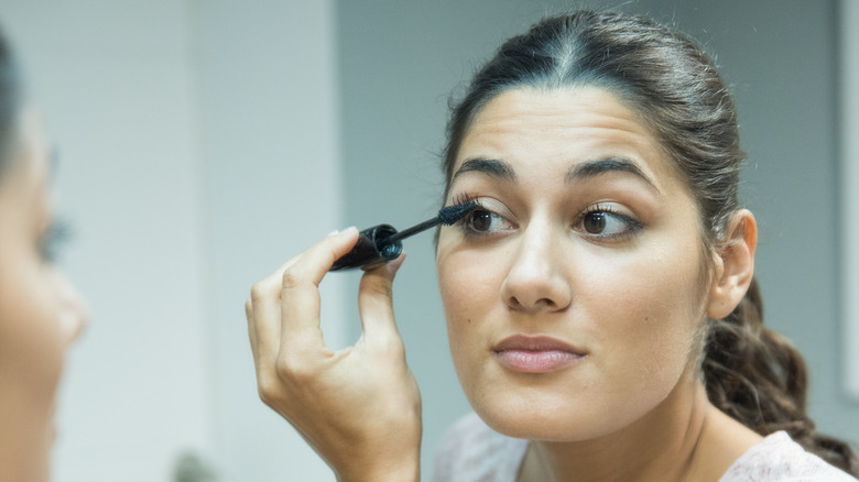 woman applying mascara while looking in mirror