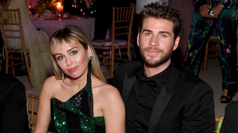 Miley Cyrus and Liam Hemsworth posing while sitting together