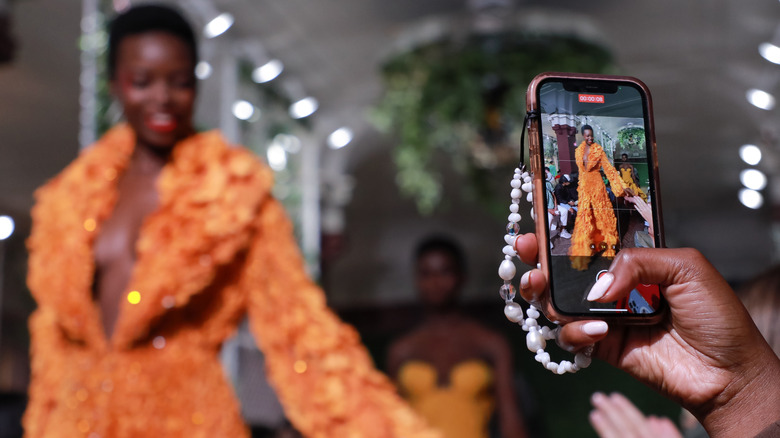 Woman walks NYFW runway as spectator takes photo on their phone