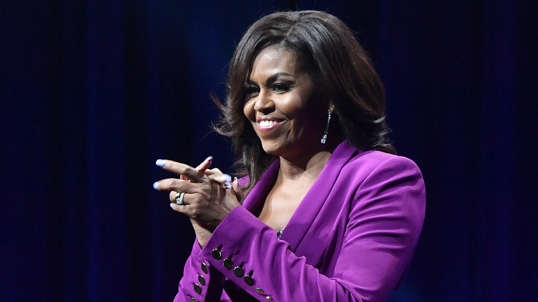 Michelle Obama wearing a purple blazer and smiling