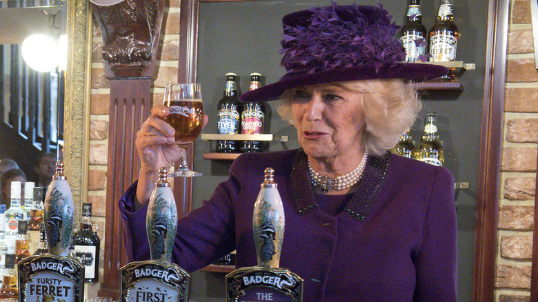 Queen Camilla talking and holding up a beer