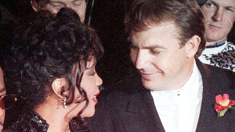 young Kevin Costner and Whitney Houston smiling at each other