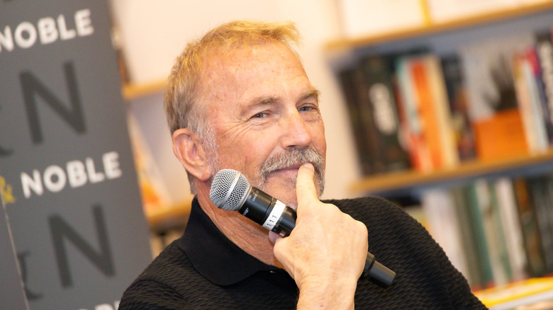 Kevin Costner with mustache holding microphone