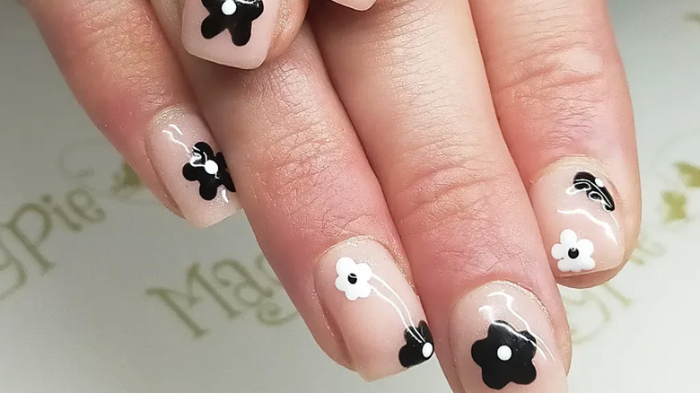 Short square nails with black and white flowers place over clear polish.