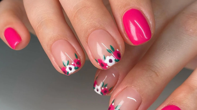 A manicure featuring white and pink flowers at the tip of two accent nails and hot pink non-accent nails.