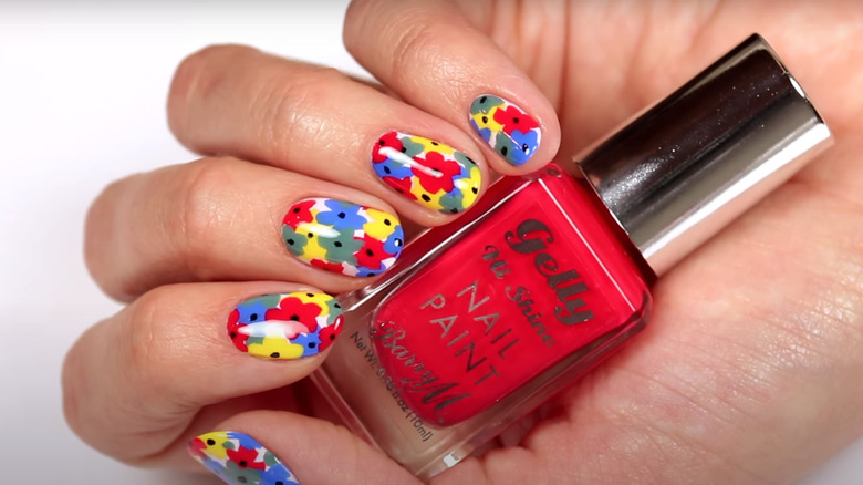 Colorful freehand nail art flowers in red, yellow, blue, and green.