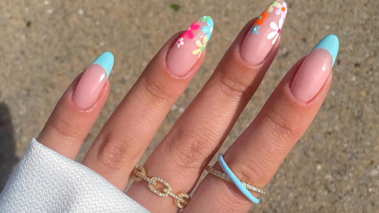 A manicure featuring colorful daisy flowers and blue French tips.