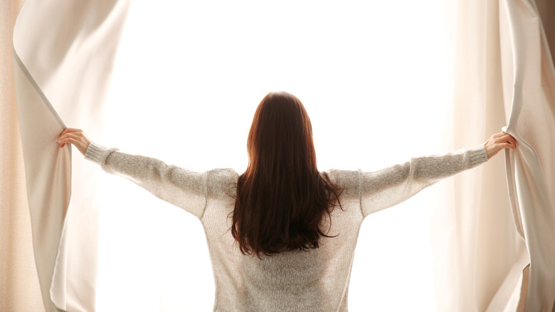 woman opening curtains