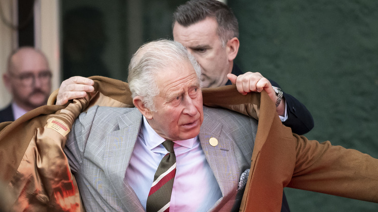 Someone helping Prince Charles put his jacket on