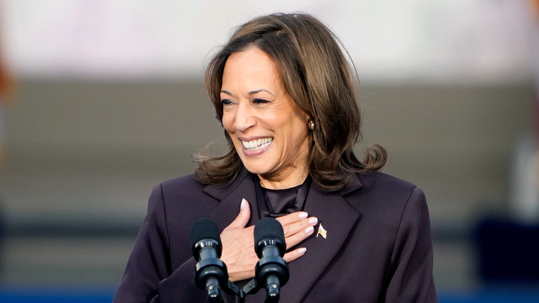 Kamala Harris grinning with her hand on her chest behind a microphone