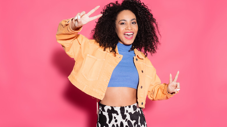 Woman wearing cow print pants and smiling while flashing a peace sign.