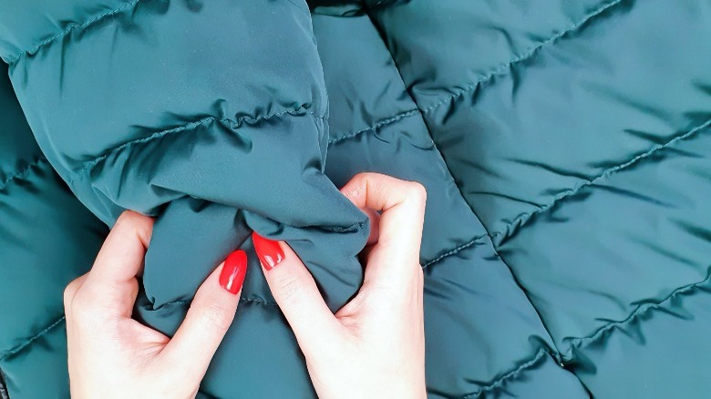 A woman squishes a puffer jacket with red nails